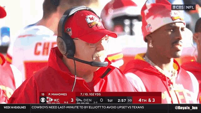 a man wearing a chiefs hat and headphones watches a game on cbs