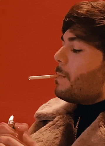 a man in a fur coat smoking a cigarette with his eyes closed
