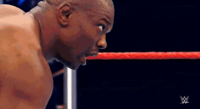 a man is standing in a wrestling ring with a red rope in the background .