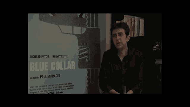 a man stands in front of a blue collar poster