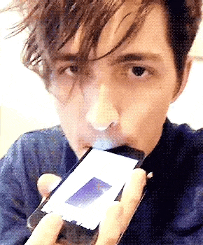 a man is smoking a cigarette while looking at a cell phone .