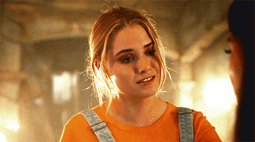 a woman wearing an orange shirt and overalls is looking at another woman .