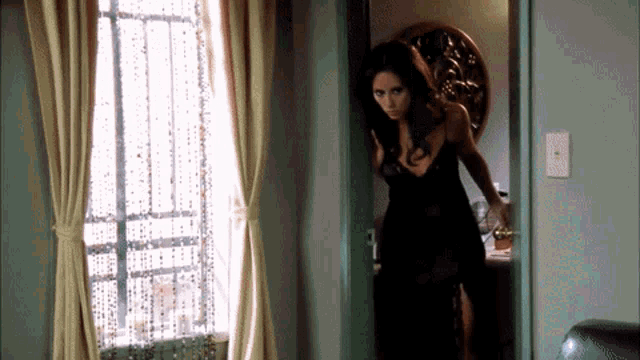 a woman in a black dress is standing in a doorway looking out a window