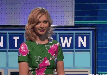 a woman in a green and pink floral top is standing in front of a board with letters on it .