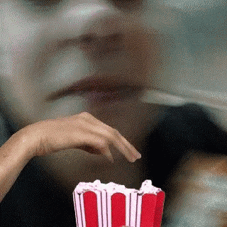 a close up of a person eating popcorn with a hand in front of their face .