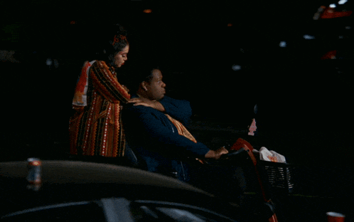 a woman standing next to a man in a wheelchair with a chevrolet car in the background