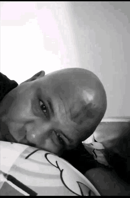 a bald man with a black spot on his forehead rests his head on a pillow