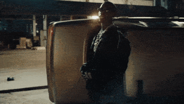 a man with a necklace around his neck is standing next to a broken car