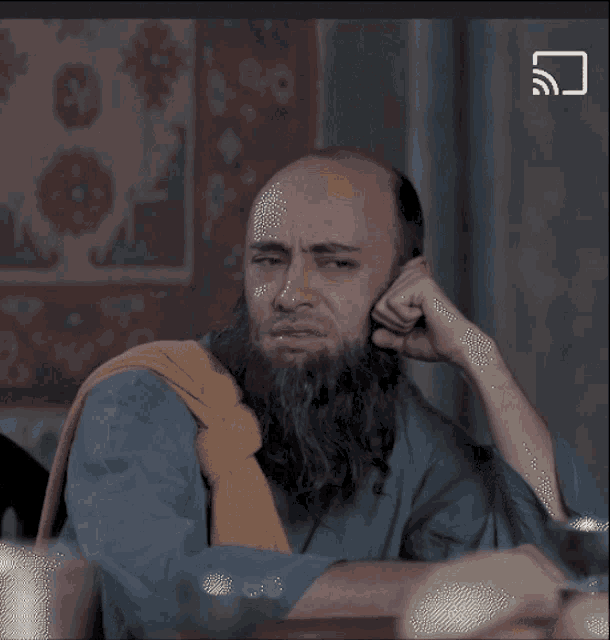 a man with a beard is sitting at a table with his hand on his face