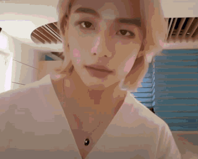 a young man with blonde hair is wearing a necklace and a white shirt .