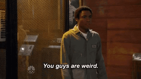 a man in a prison uniform is standing in front of a wire mesh door and says you guys are weird .