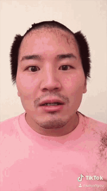 a man with a shaved head is wearing a pink shirt with tiktok written on the bottom