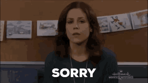 a woman in a blue sweater says sorry in front of a bulletin board