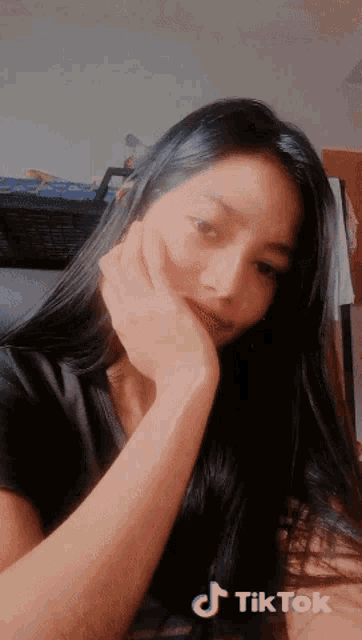 a woman with long black hair is taking a selfie with a tiktok sticker on her face