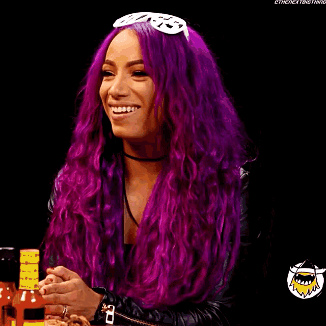 a woman with purple hair is smiling and holding a bottle of hot sauce in front of her