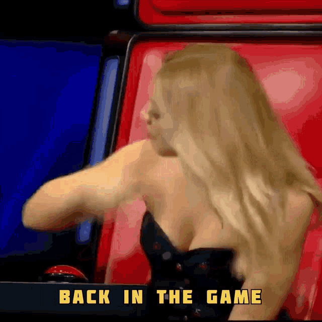 a woman in a black dress is sitting in a red chair with the words back in the game below her