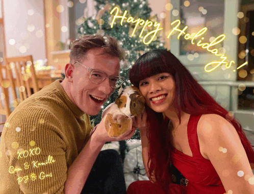 a man and woman holding a guinea pig in front of a christmas tree with happy holidays written on the bottom