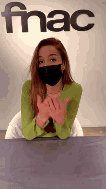 a woman wearing a mask sits in front of a sign that says fnac