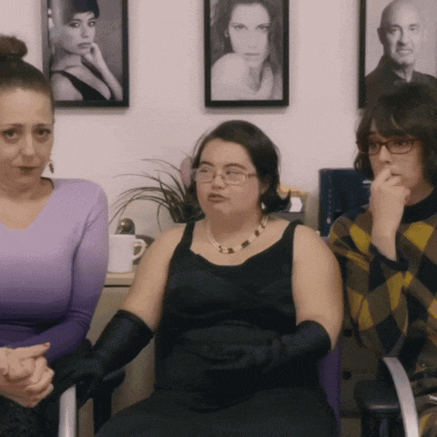 three women are sitting in chairs in front of a wall with pictures of women on it