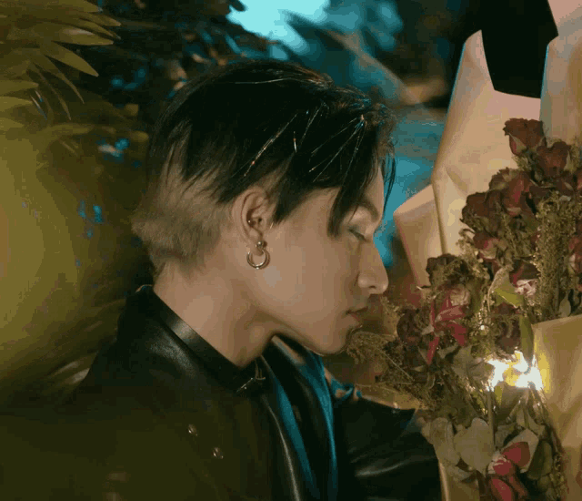 a man wearing hoop earrings smells a bouquet of red roses