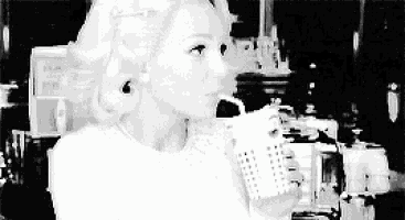 a black and white photo of a woman drinking from a white cup .