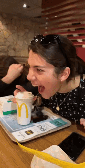 a woman is sitting at a table with a mcdonald 's cup on it