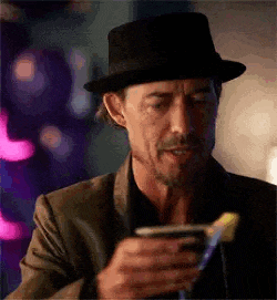 a man wearing a hat is holding a drink and looking at his phone .