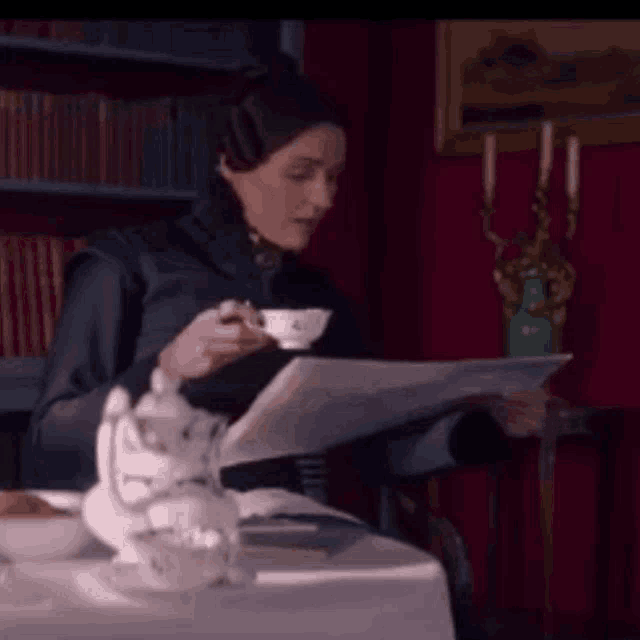 a woman is sitting at a table with a cup of tea and a newspaper .