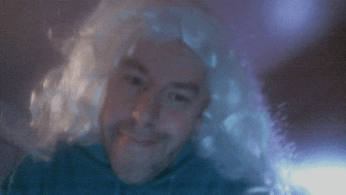 a man wearing a wig and a blue shirt is smiling