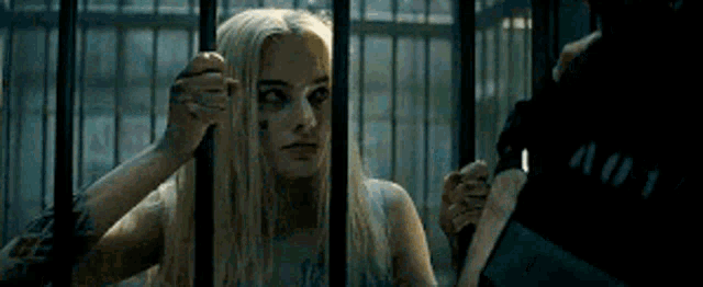 a woman is standing behind bars in a cage looking at a man .