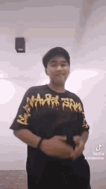 a man wearing a black t-shirt with graffiti on it is standing in front of a white wall .