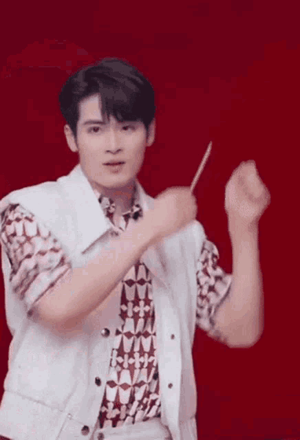 a man in a white vest and a red shirt is holding a pencil in his hand .