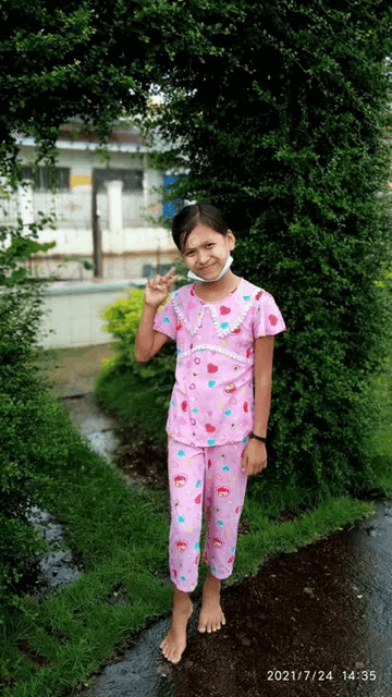 a little girl wearing a pink pajama set is standing in front of a tree and giving the peace sign