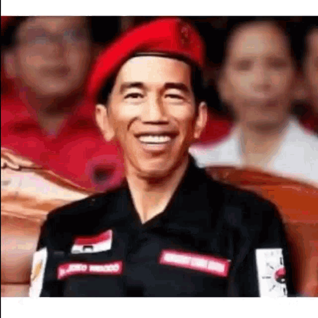 a man in a red hat is smiling in front of a crowd .