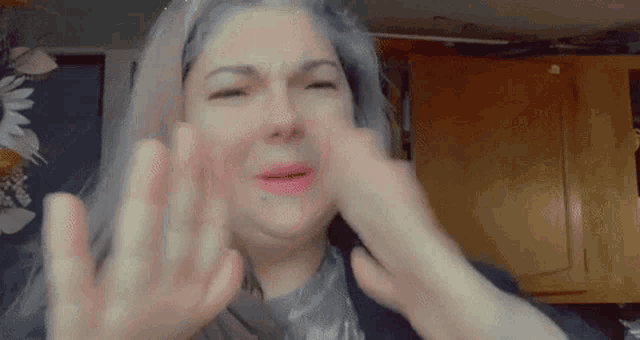 a woman with gray hair is covering her face with her hands while making a funny face .