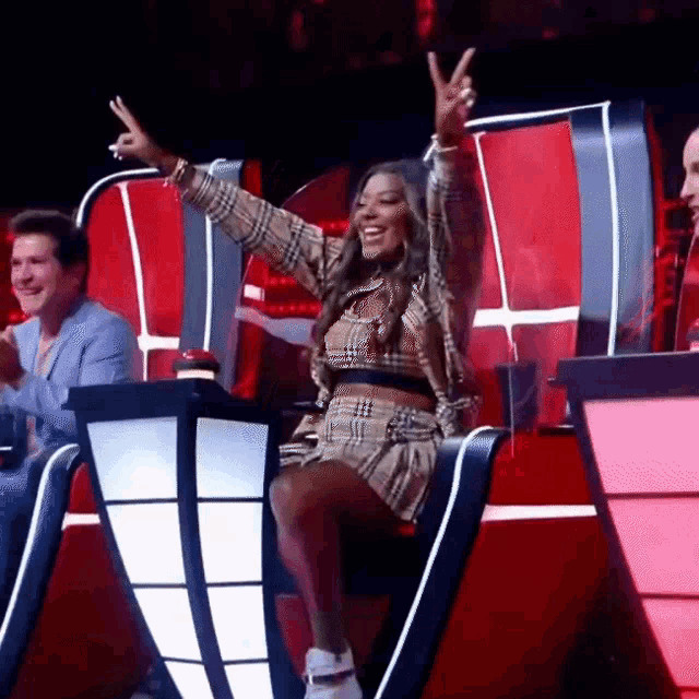 a woman is sitting in a chair with her arms in the air and giving a peace sign