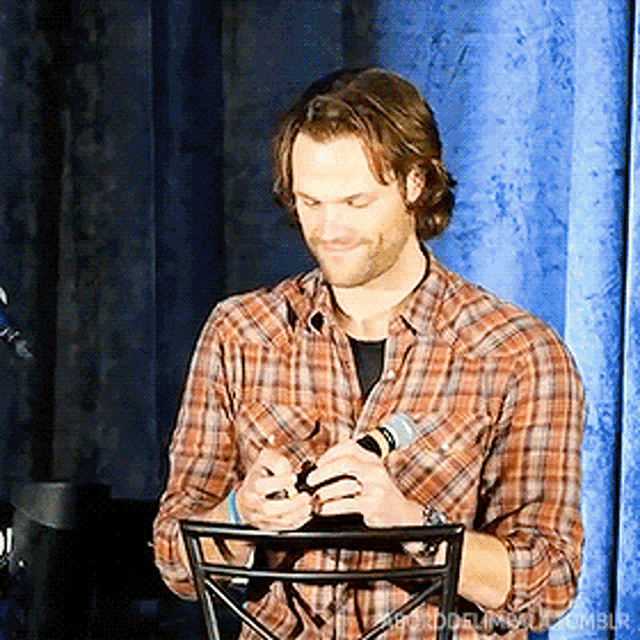 a man in a plaid shirt is holding a microphone in his hands