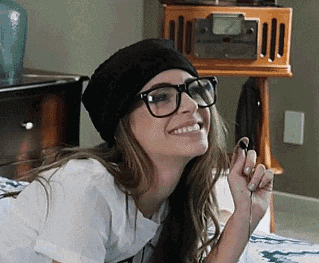 a woman wearing glasses and a beanie is smiling