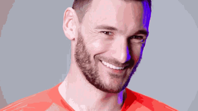 a man with a beard wearing an orange shirt smiles