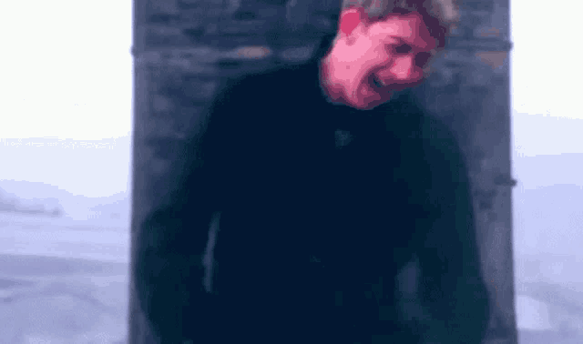 a man in a black jacket is standing in front of a stone wall and making a face .