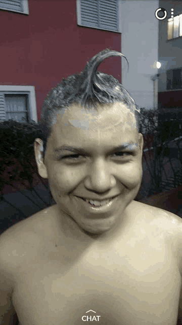 a shirtless man with a mohawk on his head is smiling and looking at the camera with a chat button below him