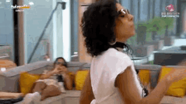 a woman is dancing in a living room while another woman sits on a couch in the background .