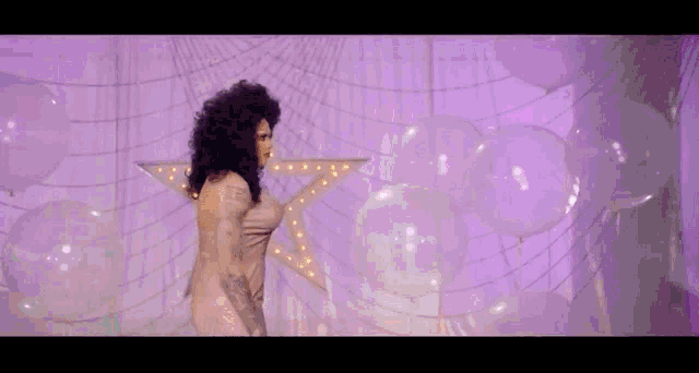 a woman in a purple dress is standing in front of a star and balloons .