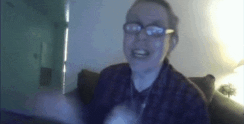 a man wearing glasses and a plaid shirt is sitting on a couch and making a funny face .