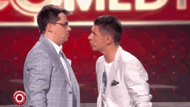 two men are looking at each other on a stage in front of a sign that says comedy
