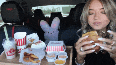 a woman in a car is eating a fried chicken sandwich from wendy 's