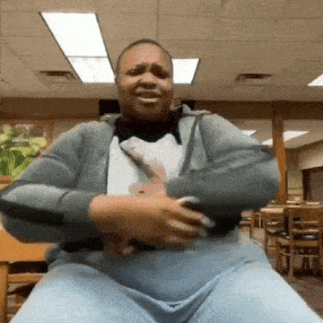 a man is sitting in a chair in a restaurant with his arms outstretched and a t-shirt on .
