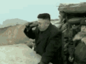 a man in a black coat is standing next to a group of soldiers on a hill .