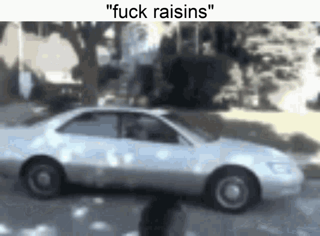 a white car is driving down a street with the words `` fuck raisins '' above it .