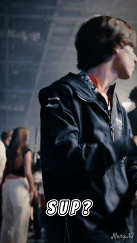 a man in a black jacket is standing in a crowd and says " sup " in white letters